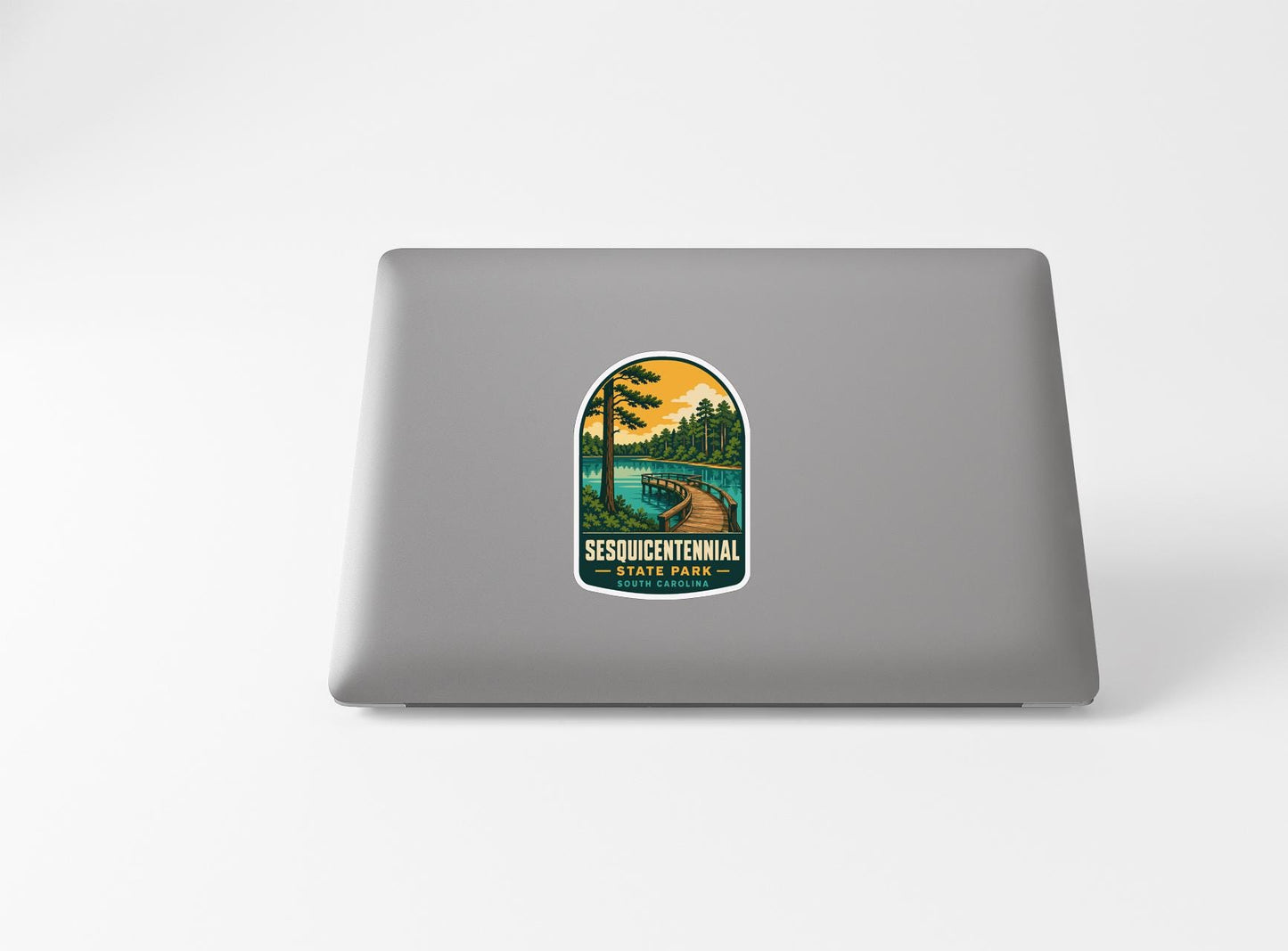 A sticker on the back of a laptop, depicting a scenic landscape with a lake, trees, and a path leading through the wooded area.