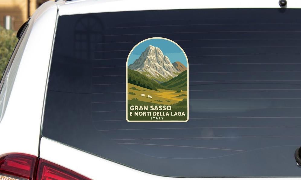 A sticker on the rear window of a car depicting a mountain landscape with a small herd of sheep grazing in the foreground.