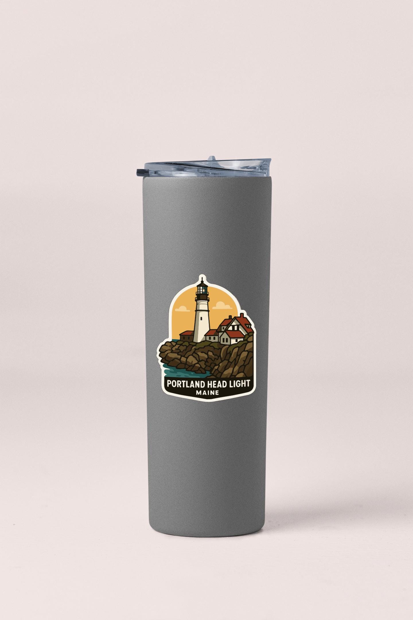 A gray insulated tumbler with a sticker depicting a lighthouse and the text "P Portland Head Light Maine" printed on it.