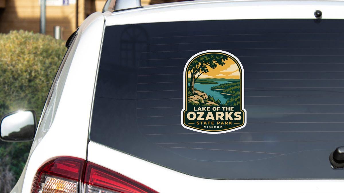 A sticker on the rear window of a white vehicle, depicting a scenic landscape with a lake and mountains.