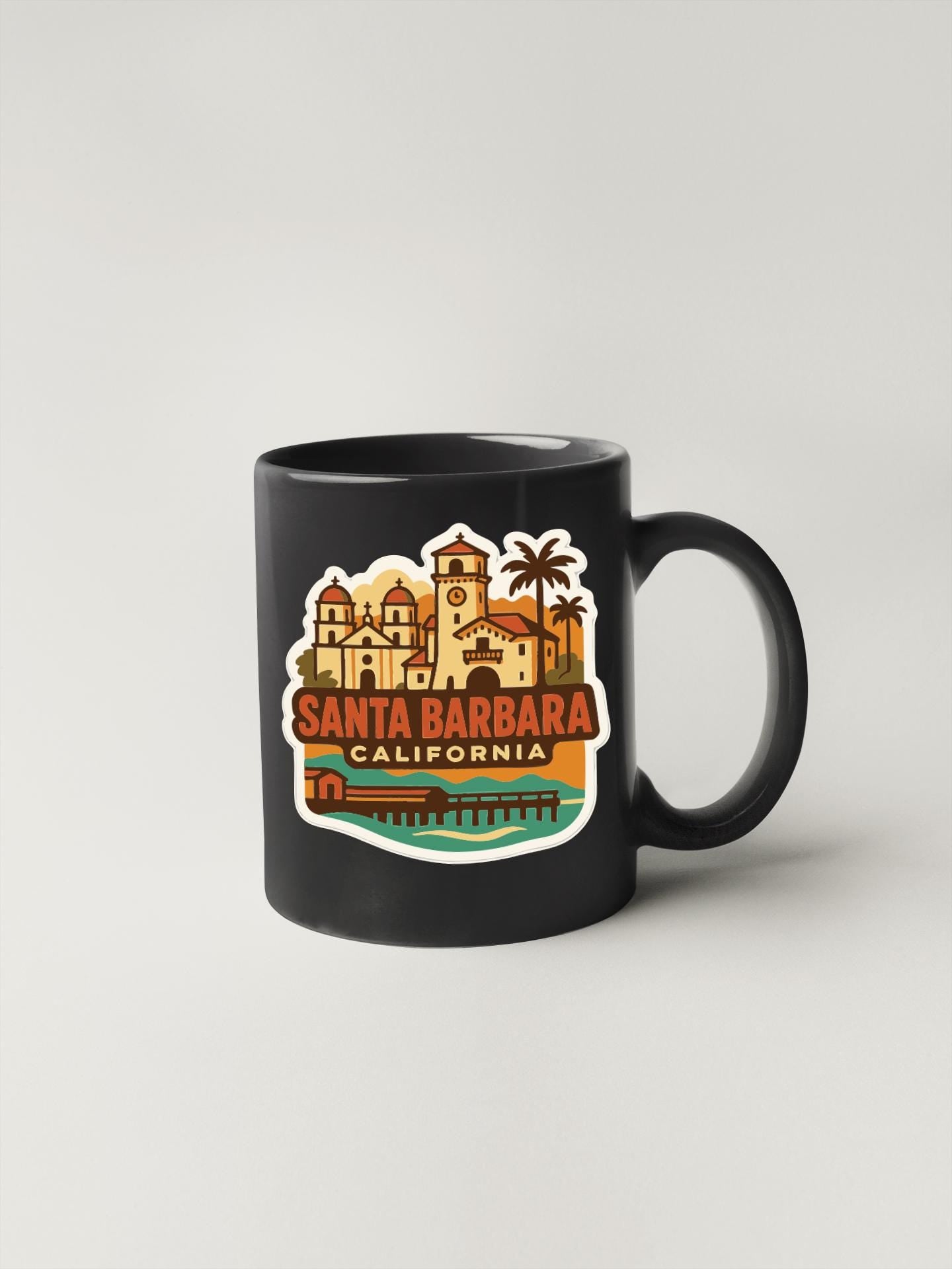 A black coffee mug with a colorful sticker depicting Santa Barbara, California.