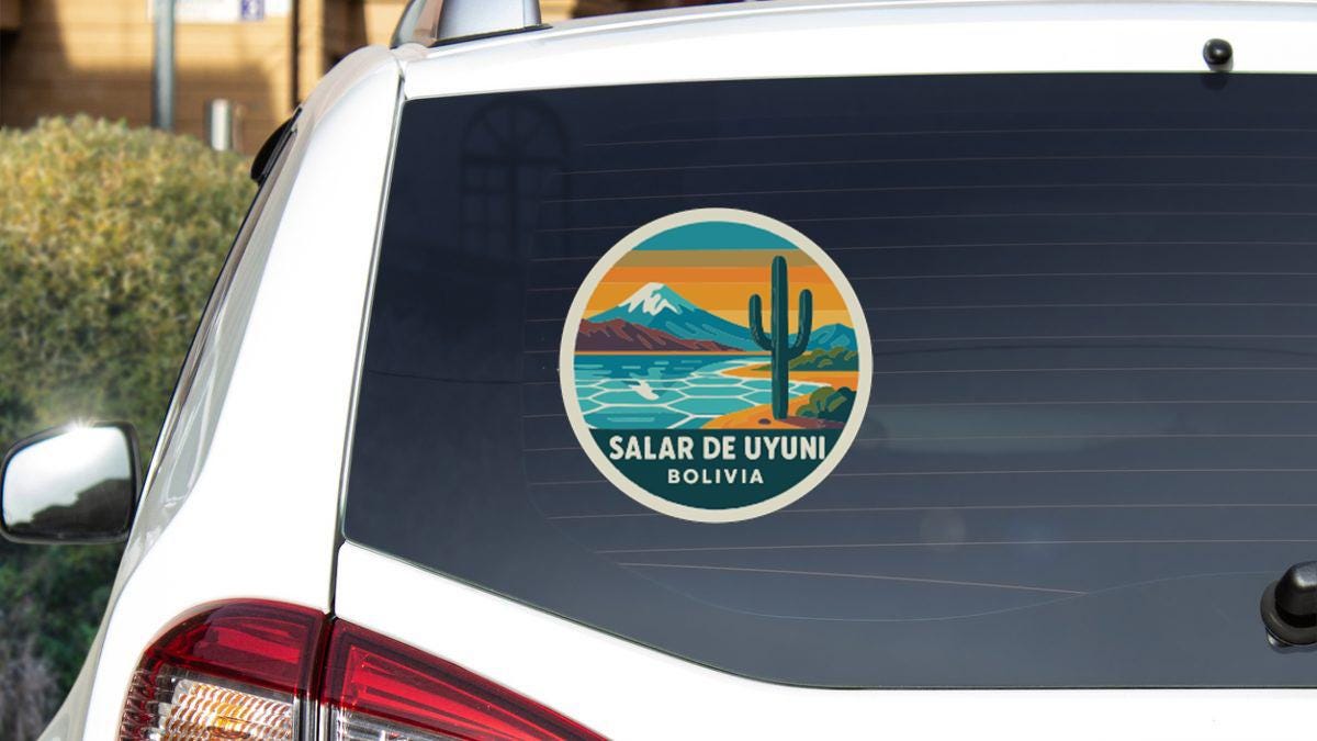 a sticker on the rear window of a white car, depicting a scenic landscape with mountains, a desert, and a cactus.