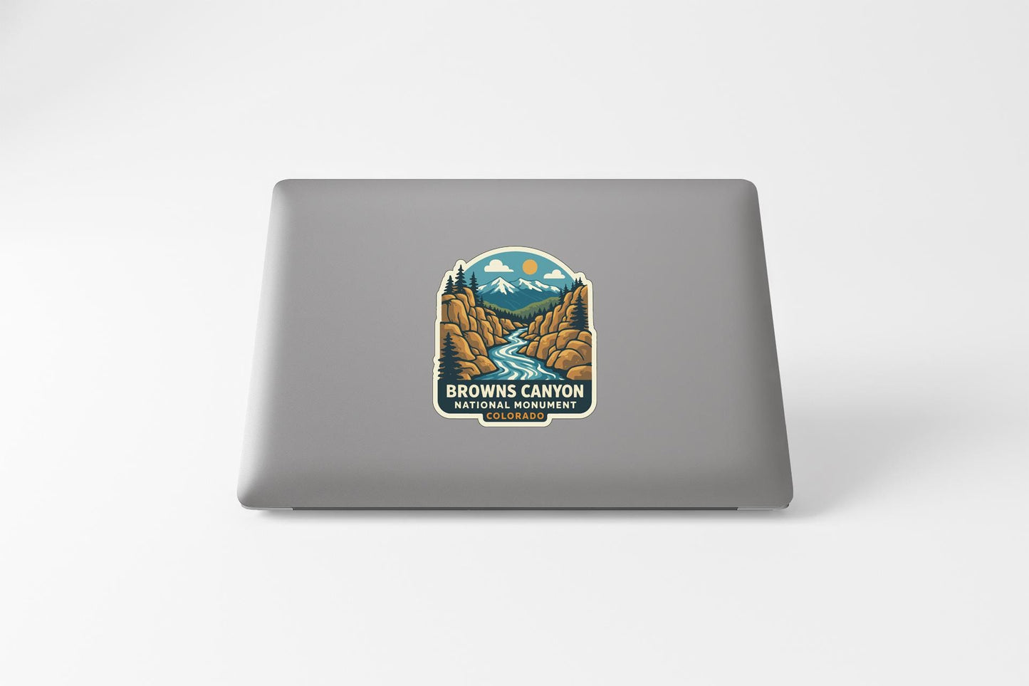 A sticker on the back of a laptop, depicting a scenic landscape with mountains, a river, and a forest.