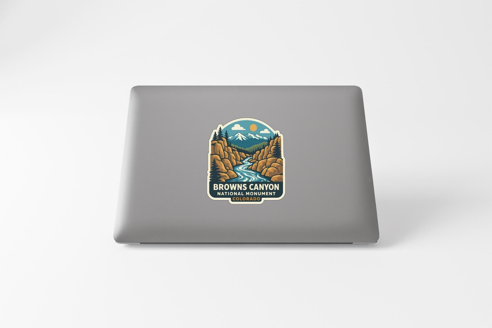 A sticker on the back of a laptop, depicting a scenic landscape with mountains, a river, and a forest.