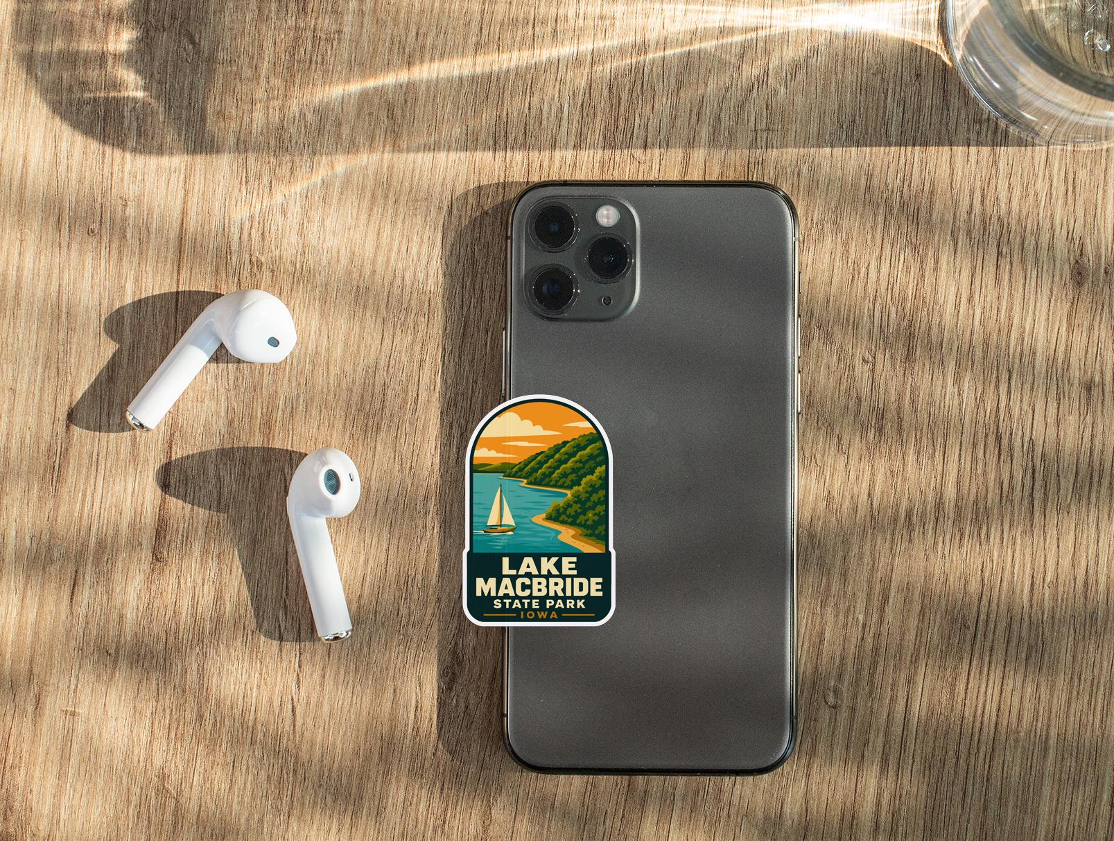 a smartphone with a sticker on it, along with a pair of white earbuds and a glass of water on a wooden surface.