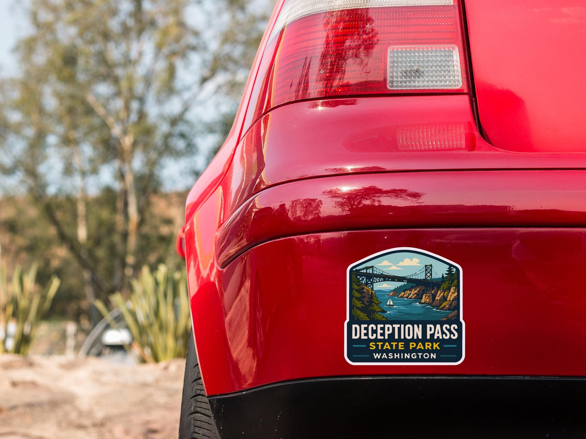 the rear end of a red car with a sticker on the back window that says "Deception Pass State Park Washington".