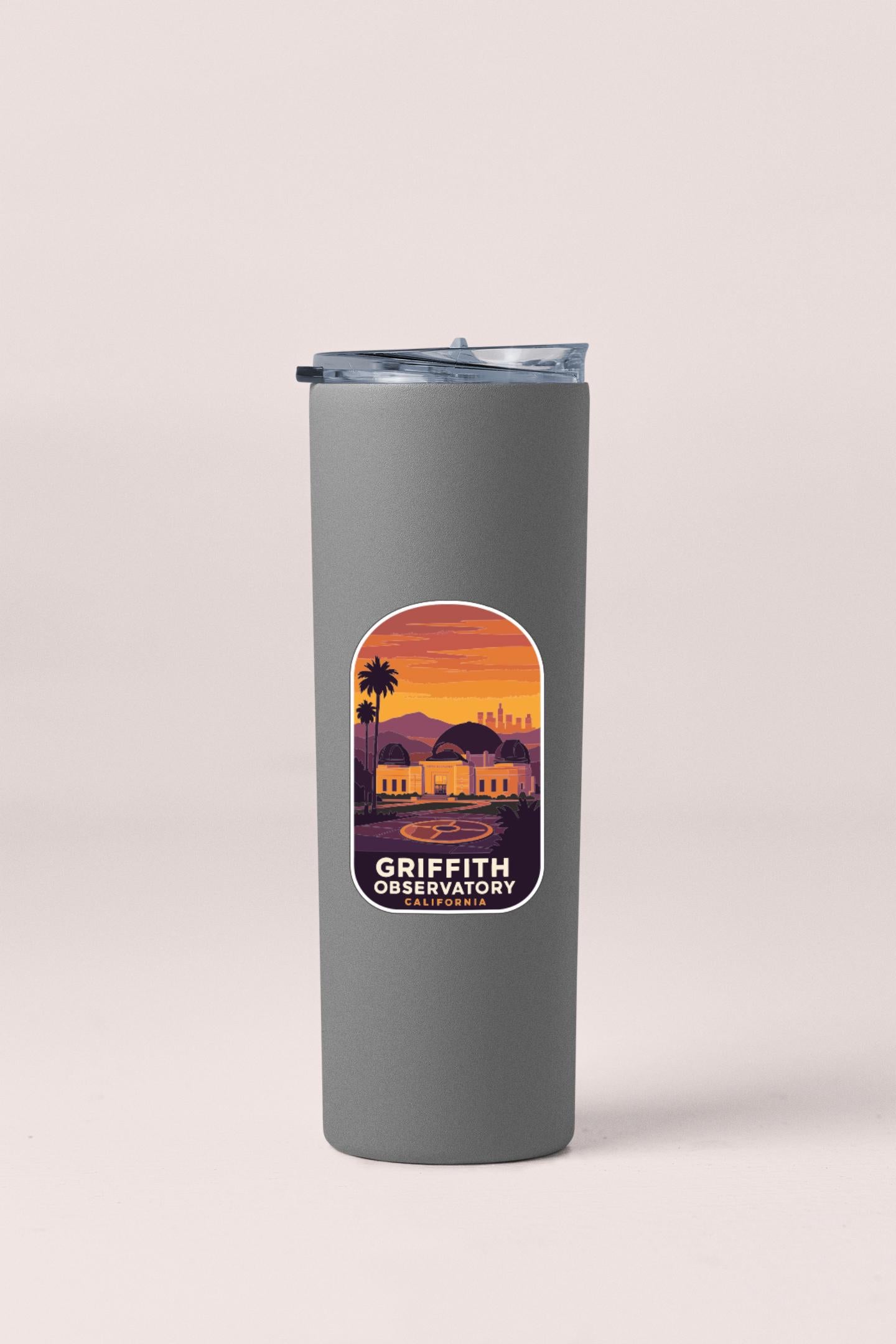 A gray insulated tumbler with a label that features an illustration of a sunset over a city skyline.