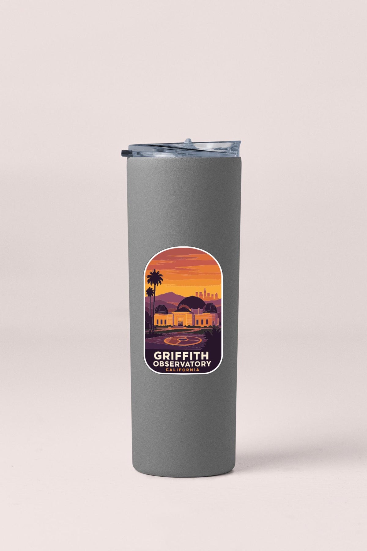 A gray insulated tumbler with a label that features an illustration of a sunset over a city skyline.