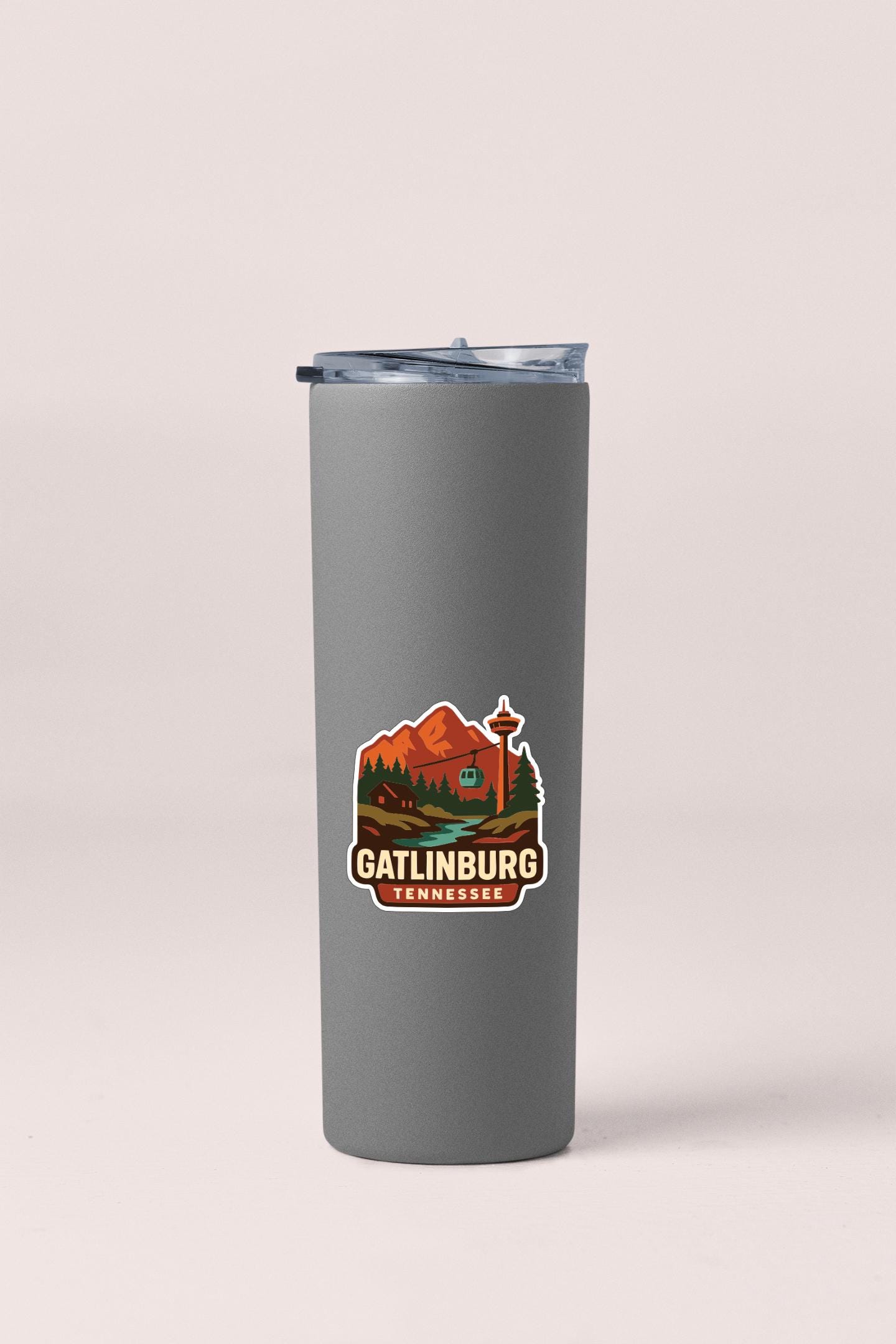 A gray insulated tumbler with a sticker depicting a scenic mountain landscape and the text "Gatlinburg, Tennessee".
