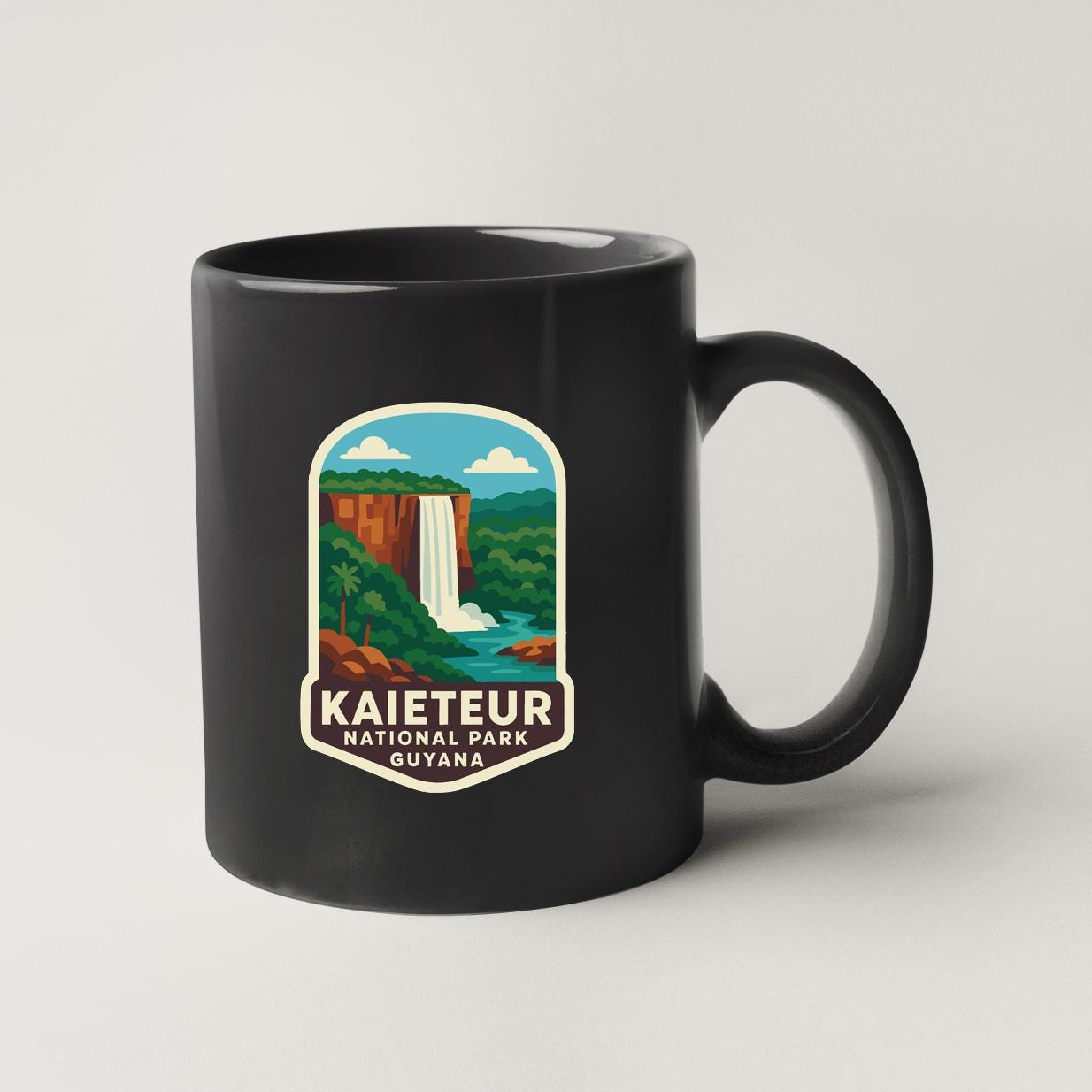 A black coffee mug with a graphic design depicting a waterfall and lush greenery, along with the text "KAIETEUR NATIONAL PARK GUYANA".