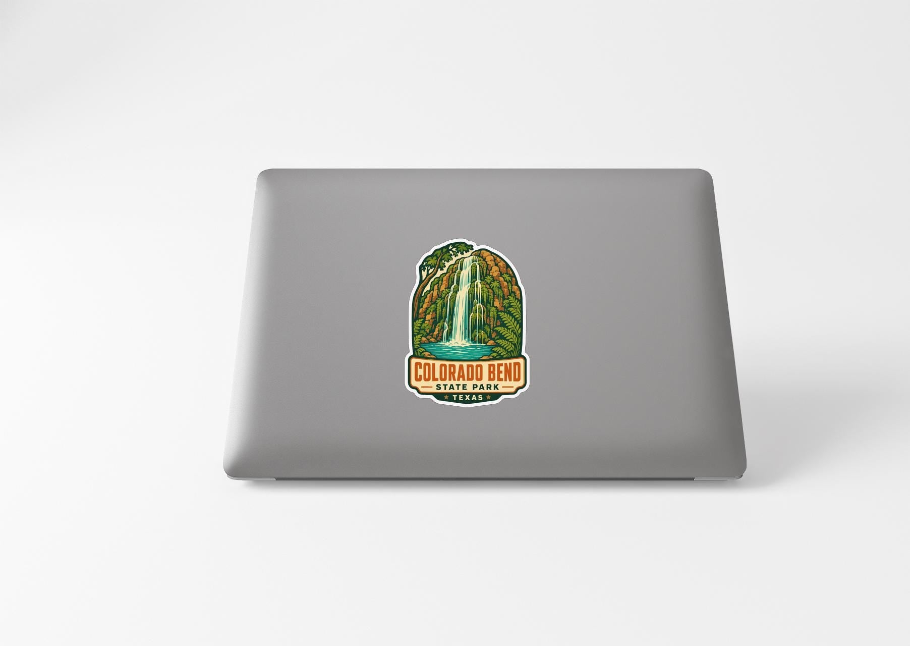 A sticker on the back of a laptop, depicting a waterfall surrounded by lush greenery.
