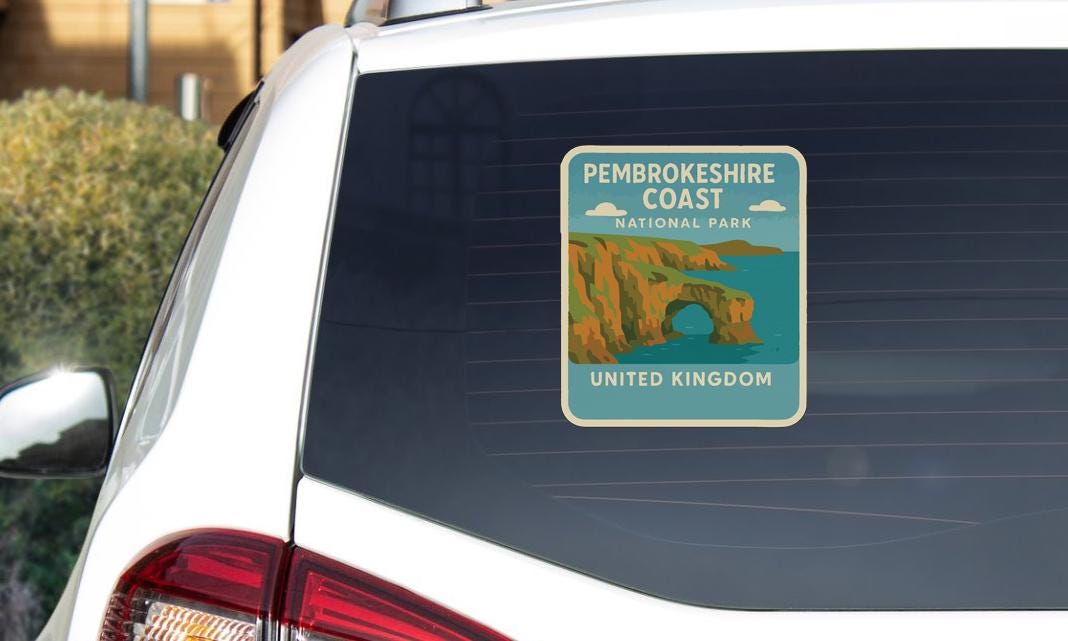 A sticker on the rear window of a car, depicting a scenic coastal landscape with cliffs and a body of water.