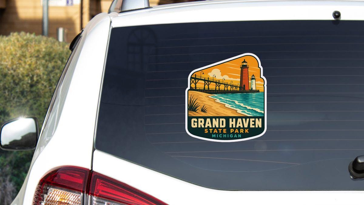 A sticker on the rear window of a white vehicle, depicting a scenic view of Grand Haven State Park in Michigan.
