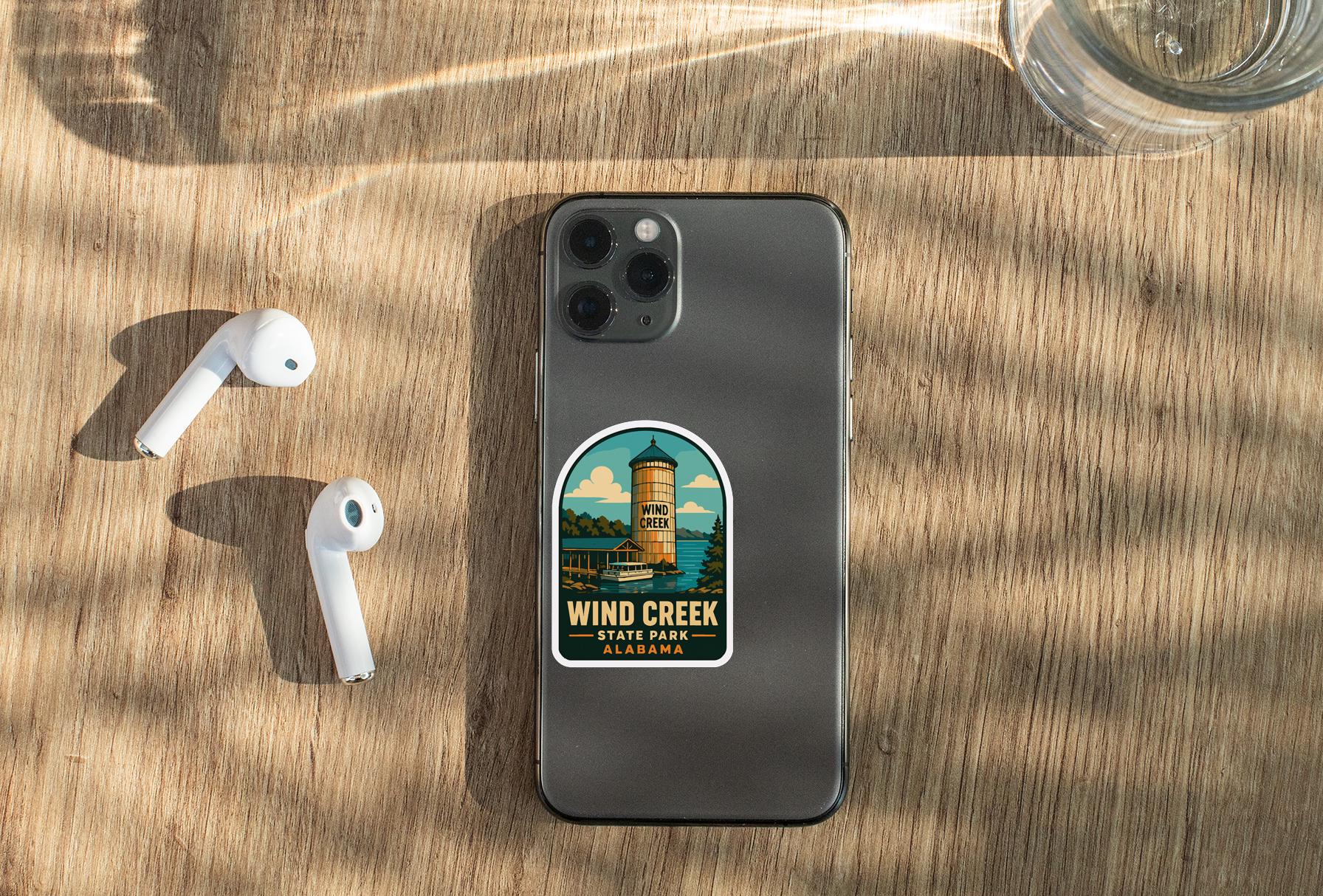 a smartphone with a sticker on the back, placed on a wooden surface alongside a pair of white earbuds and a glass of water.
