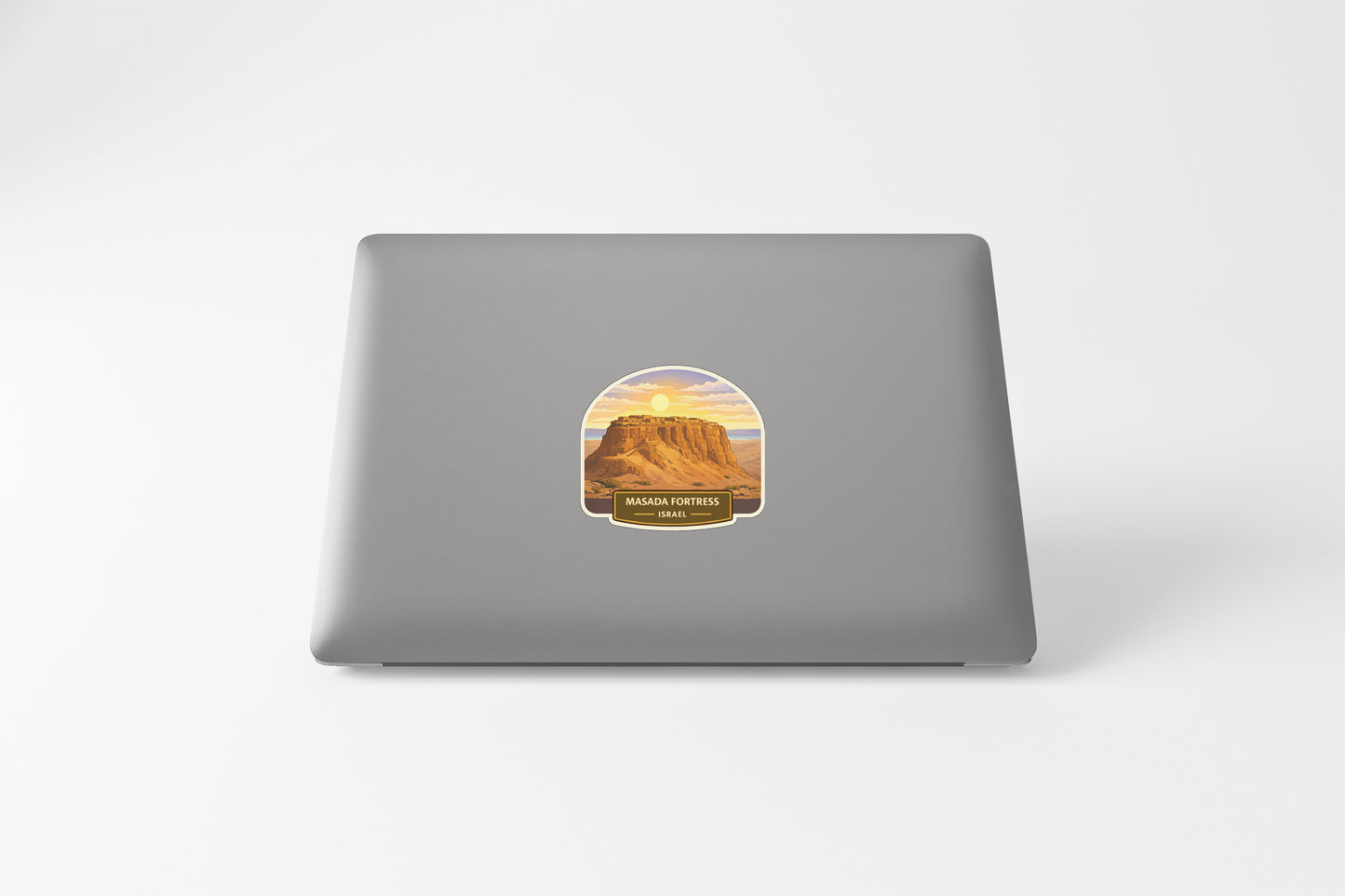A sticker depicting a mountain landscape with a sunset in the background is placed on the back of a laptop computer.
