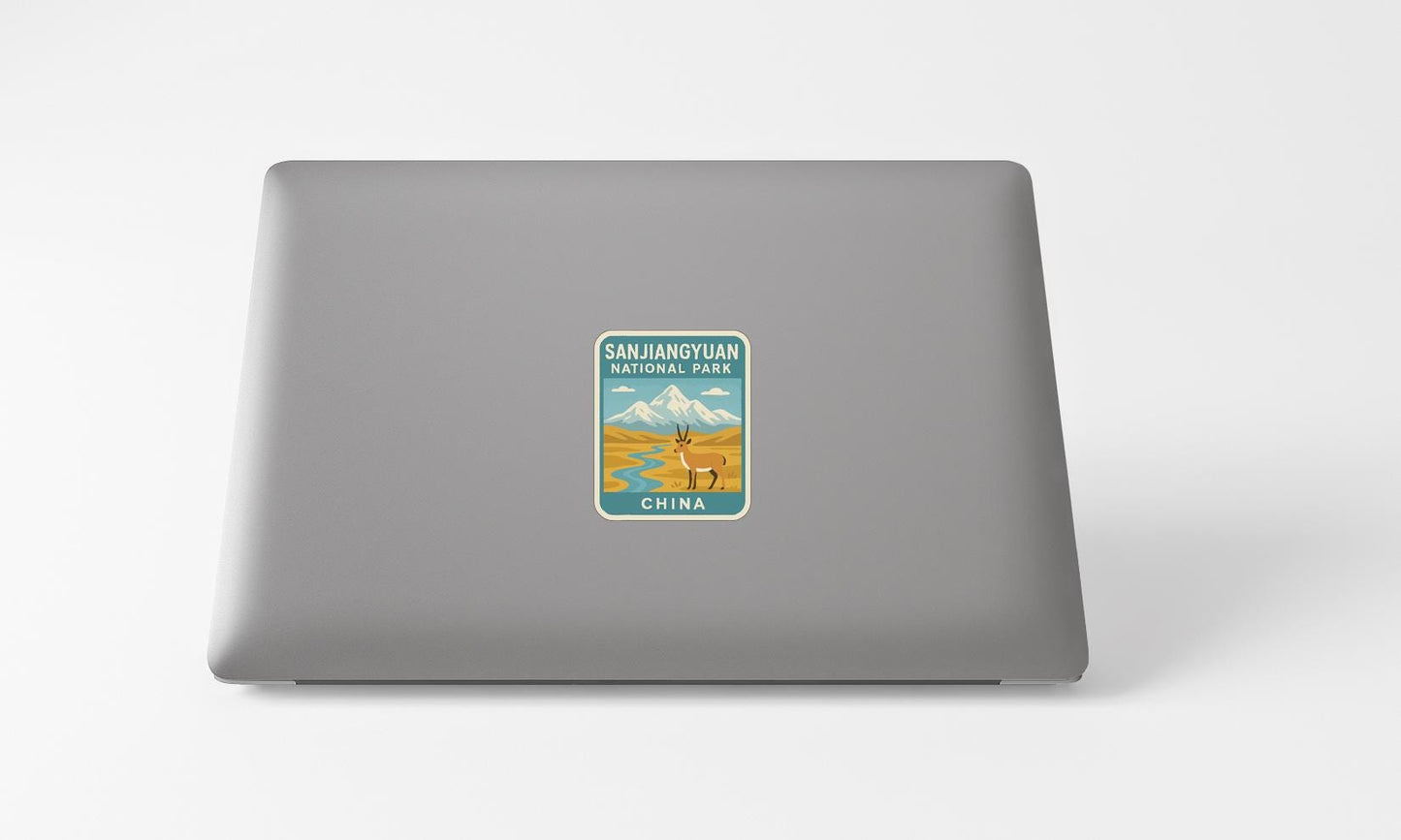 A sticker on the back of a laptop, depicting a scenic landscape with mountains and a river.