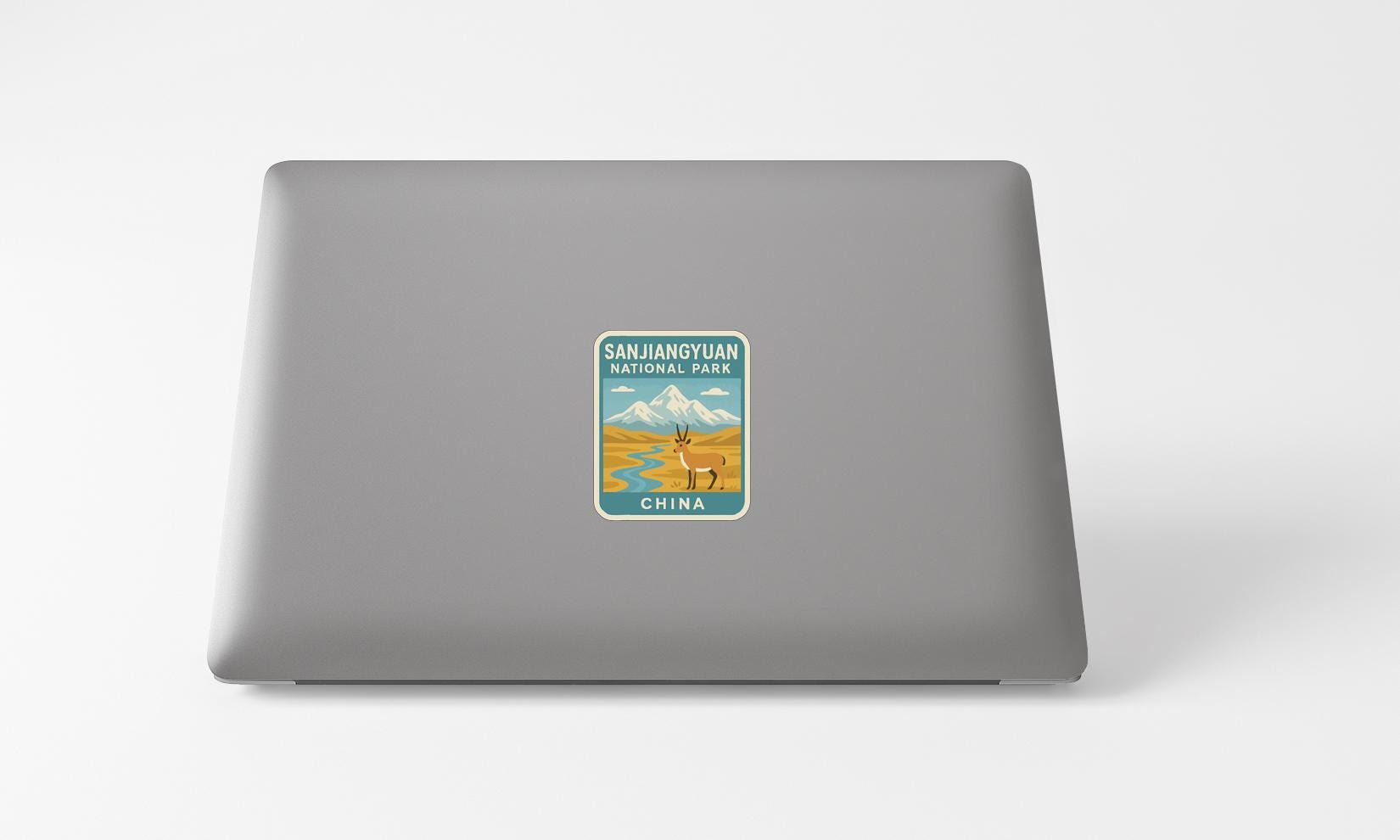 A sticker on the back of a laptop, depicting a scenic landscape with mountains and a river.