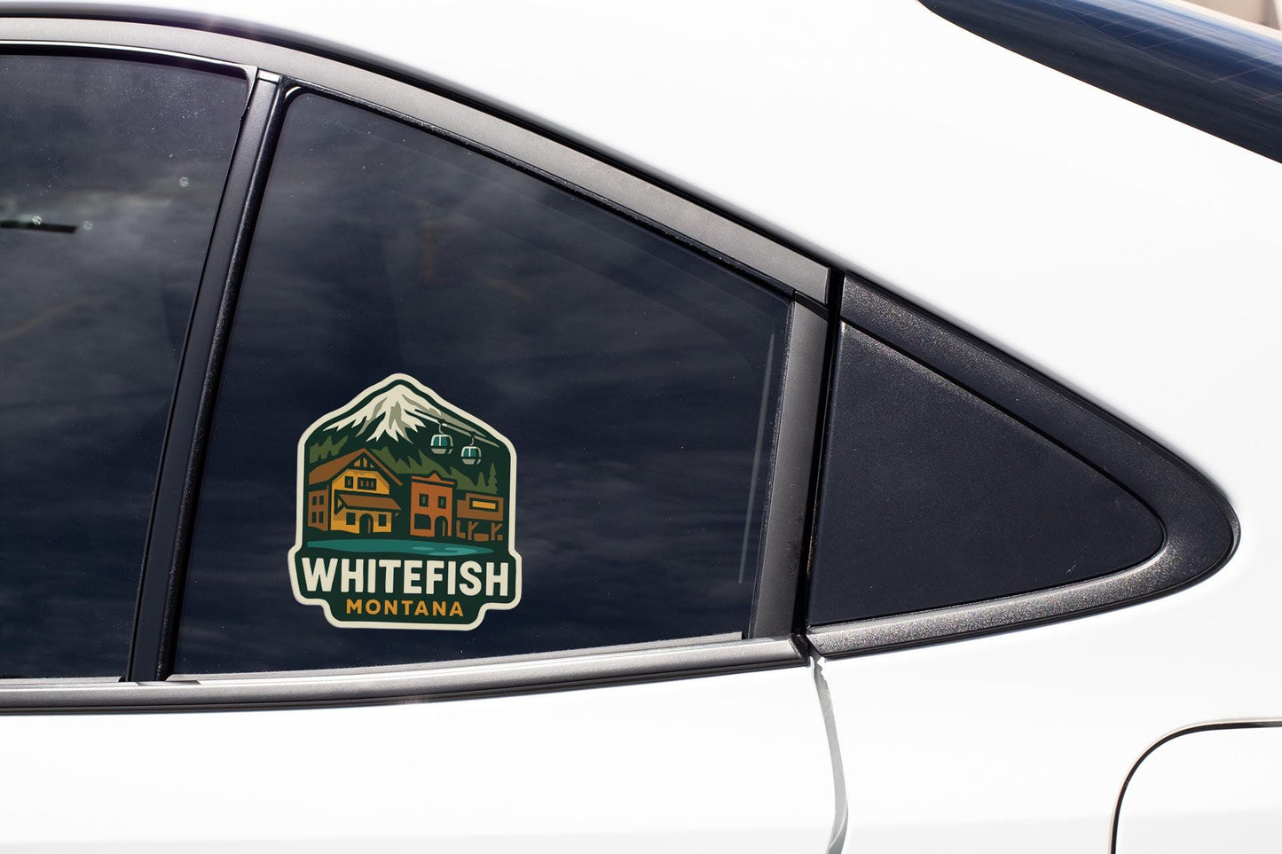 A sticker on the side of a car window, featuring a mountain landscape with a lodge and text that says "WHITEFISH MORTANA".