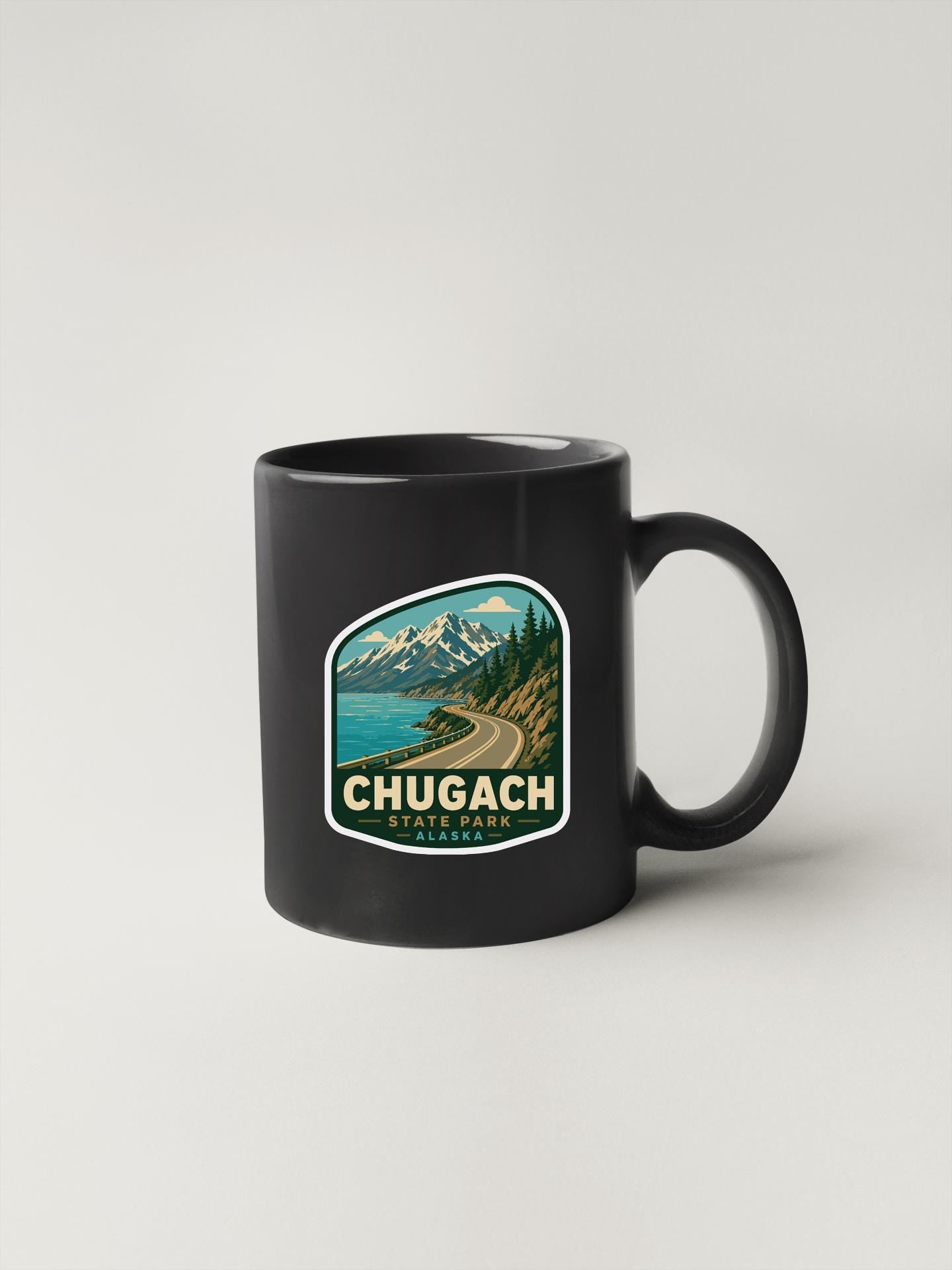 A black coffee mug with a sticker depicting a scenic mountain landscape and the text "CHUGACH STATE PARK, WA".