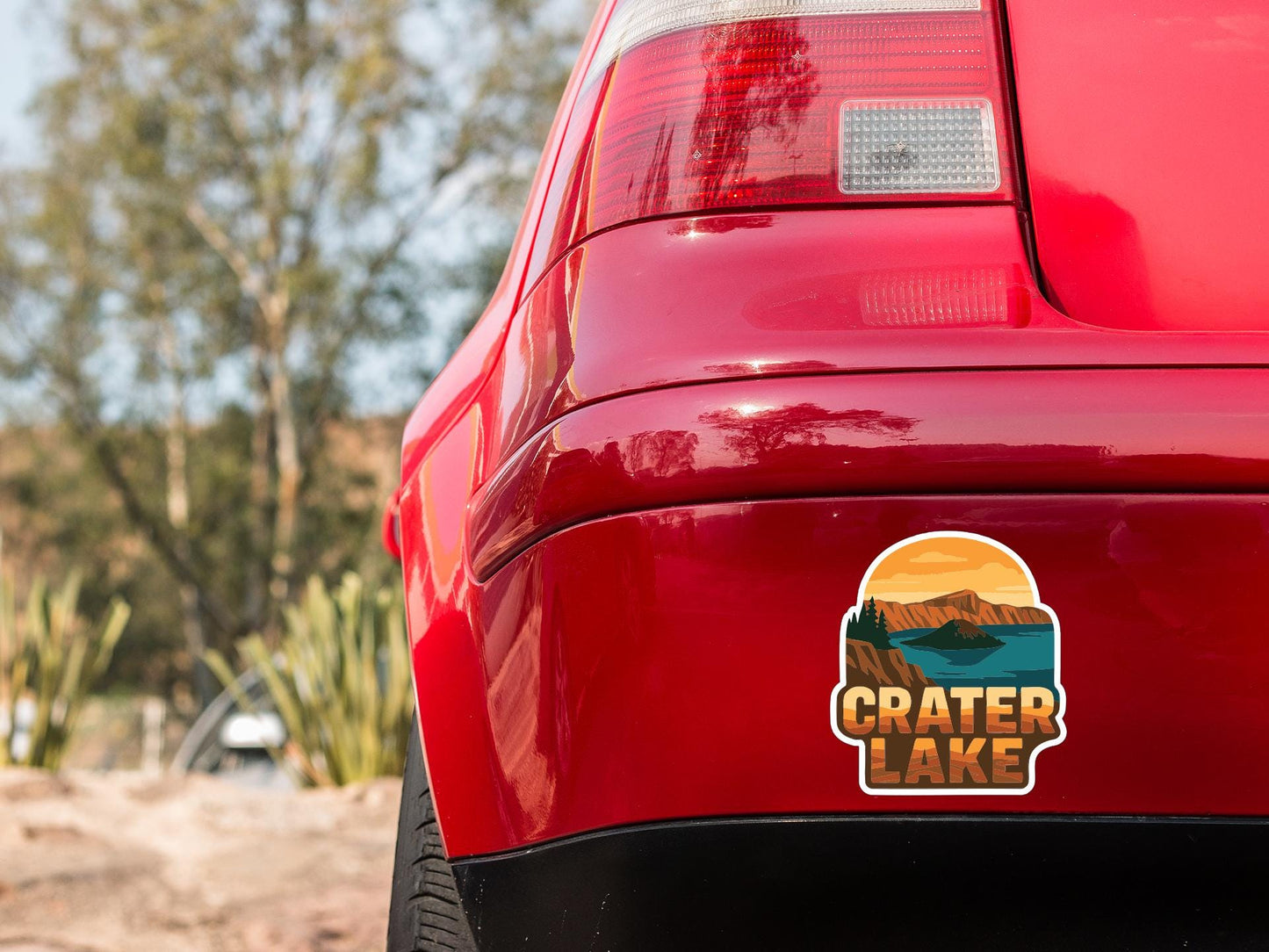 the rear end of a red car with a sticker on the bumper that says "Crater Lake".