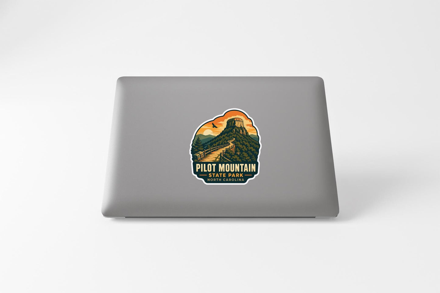 A sticker on the back of a laptop that features a mountain landscape with a road leading up to a tower.