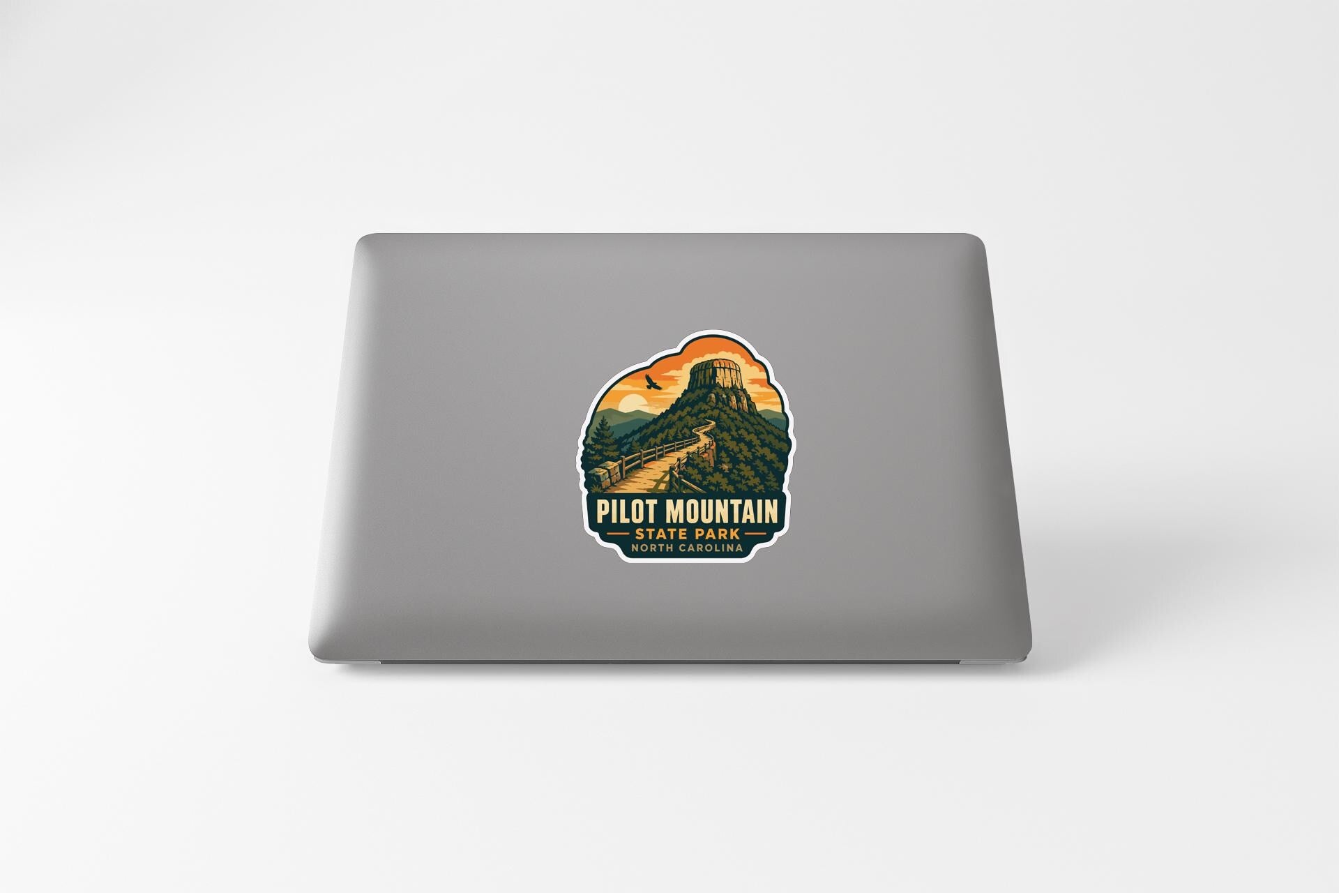 A sticker on the back of a laptop that features a mountain landscape with a road leading up to a tower.