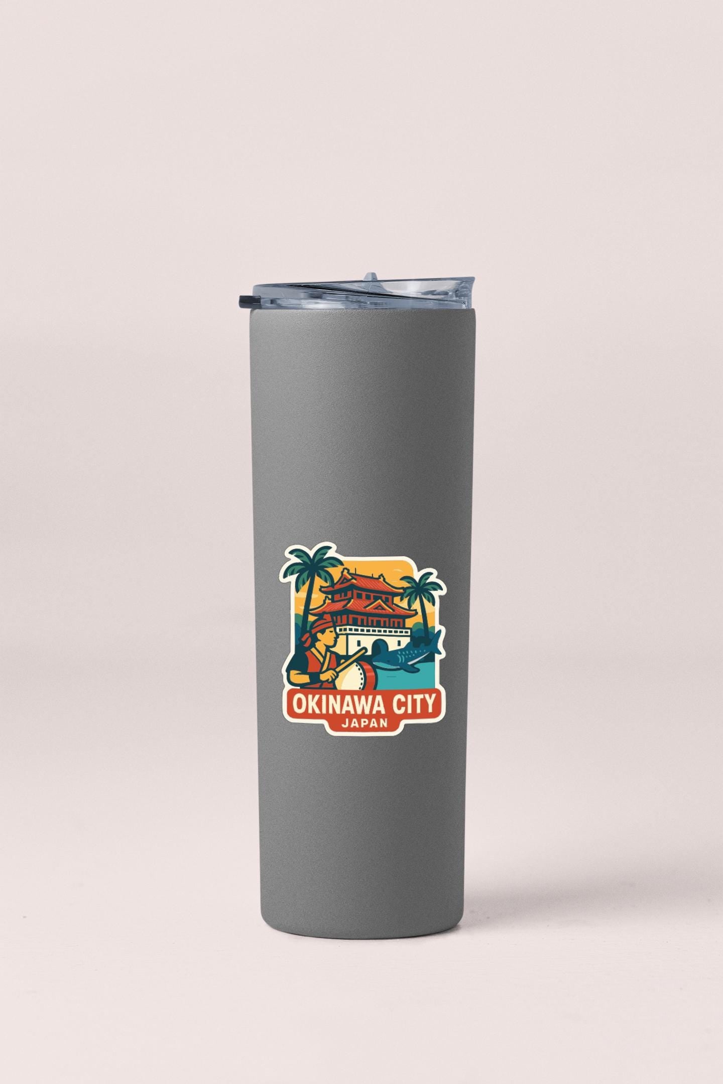 A gray insulated tumbler with a sticker depicting a tropical scene and the text "OKINAWA CITY JAPAN".