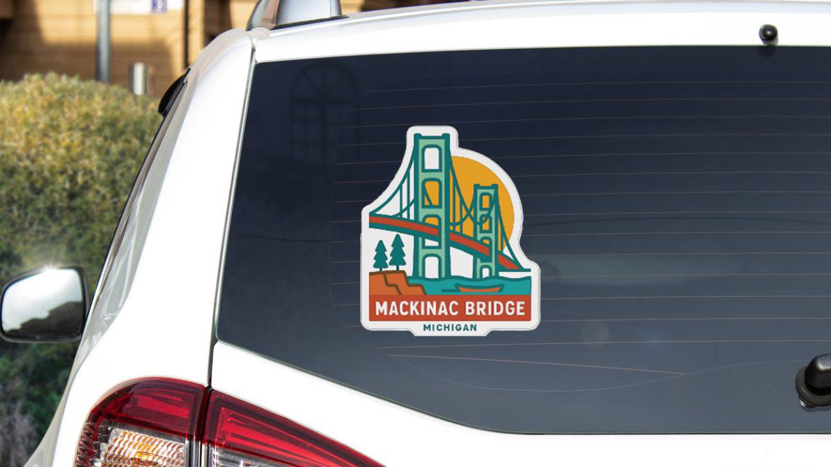 A sticker on the rear window of a white car, depicting the Mackinac Bridge in Michigan.