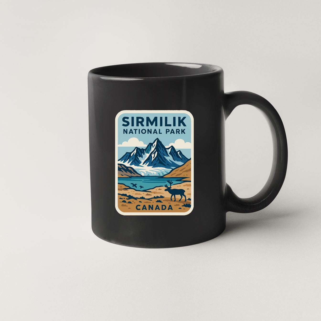 A black coffee mug with a sticker depicting a scenic landscape of mountains, a lake, and wildlife, including a moose.