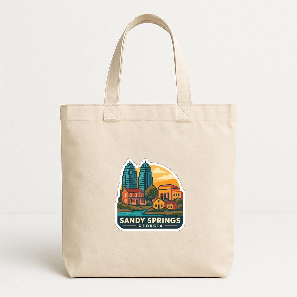 A beige tote bag with a printed design depicting a city skyline and the text "SANDY SPRINGS GEORGIA".