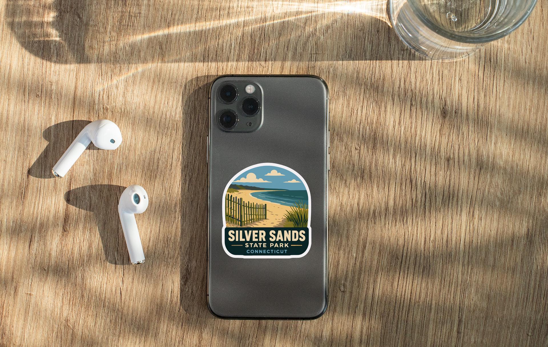 a smartphone with a sticker on it, placed on a wooden surface alongside a pair of white earbuds and a glass of water.