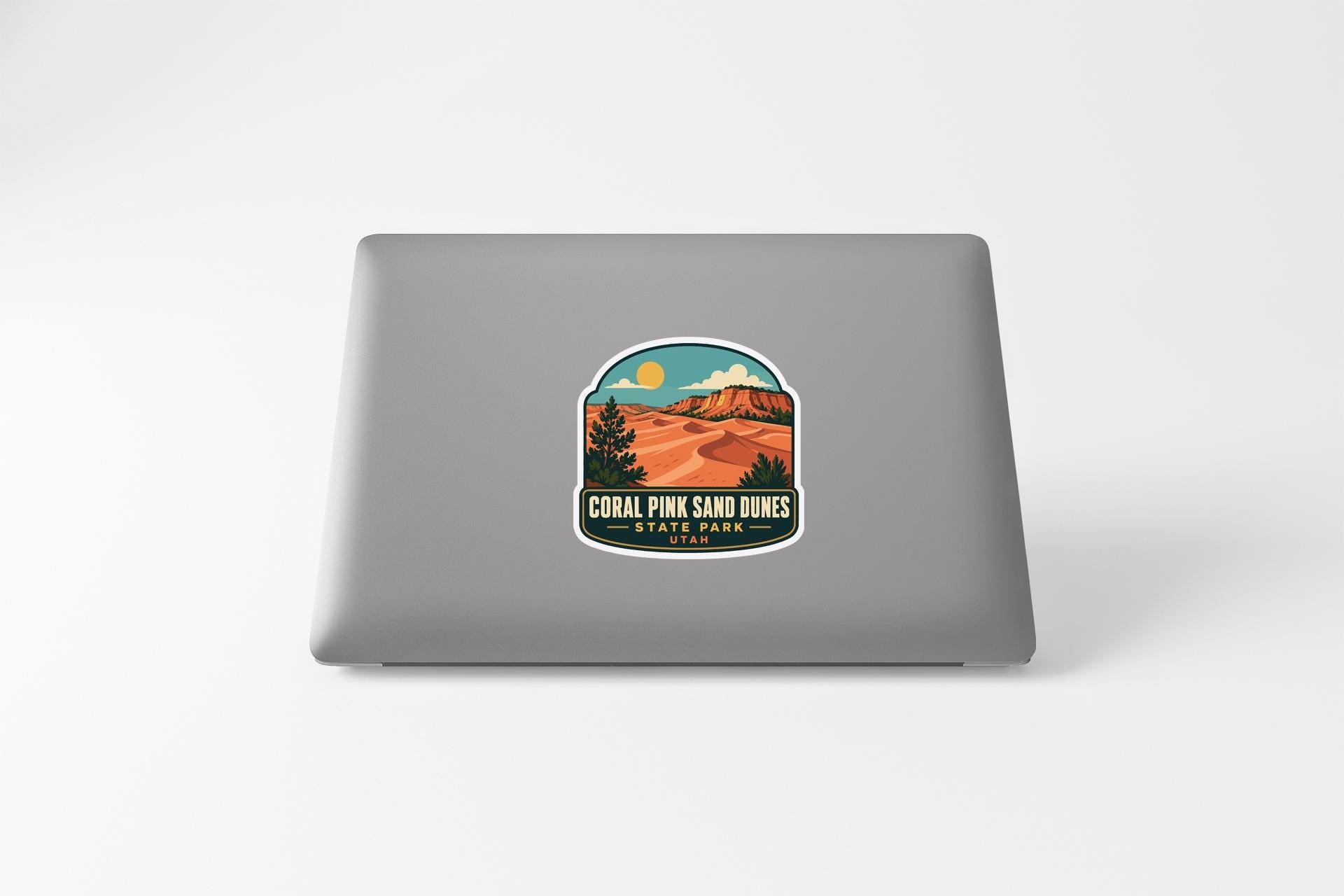A sticker on the back of a laptop, depicting a scenic landscape with mountains, trees, and a desert-like environment.