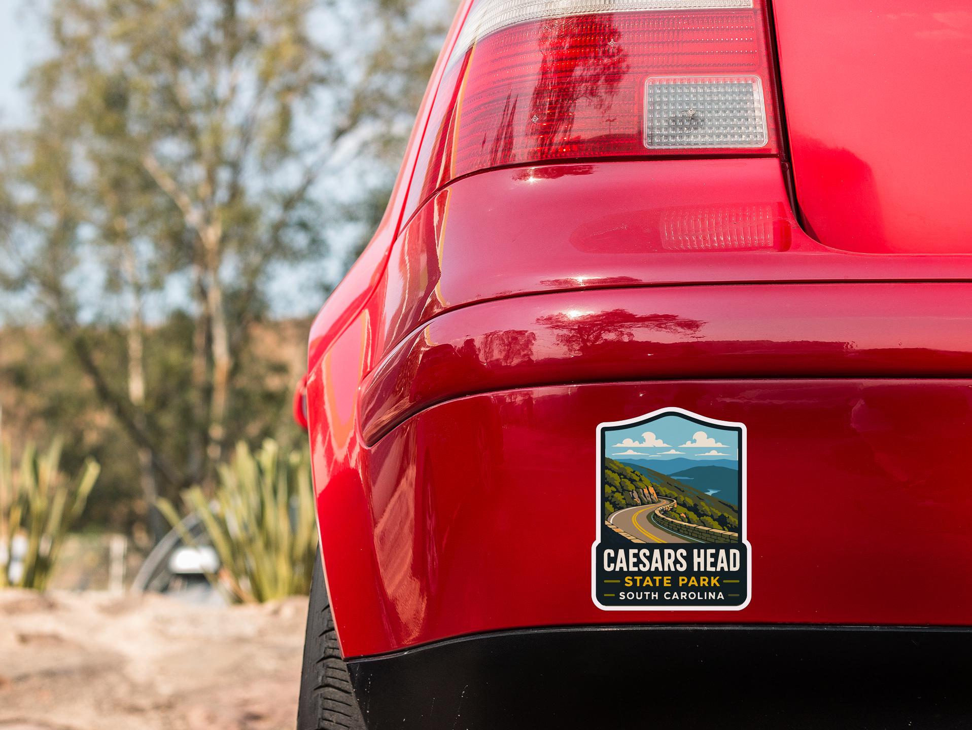 the rear end of a red car with a CAESARS HEAD State Park South Carolina license plate sticker on the rear bumper.