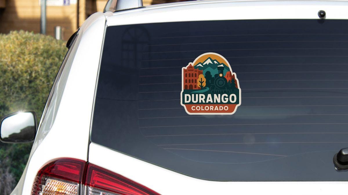 A sticker on the rear window of a white car, displaying the text "DURANGO COLORADO" along with an illustration of a train and buildings.