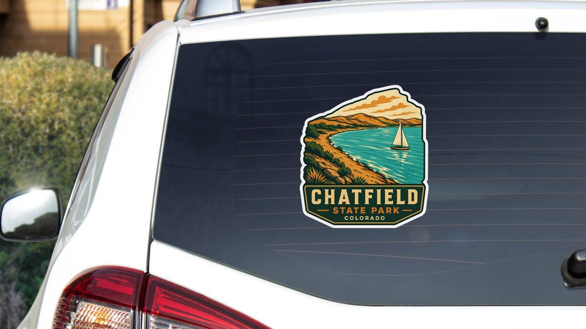 A sticker on the rear window of a white vehicle, depicting a scenic landscape with a sailboat on a lake.