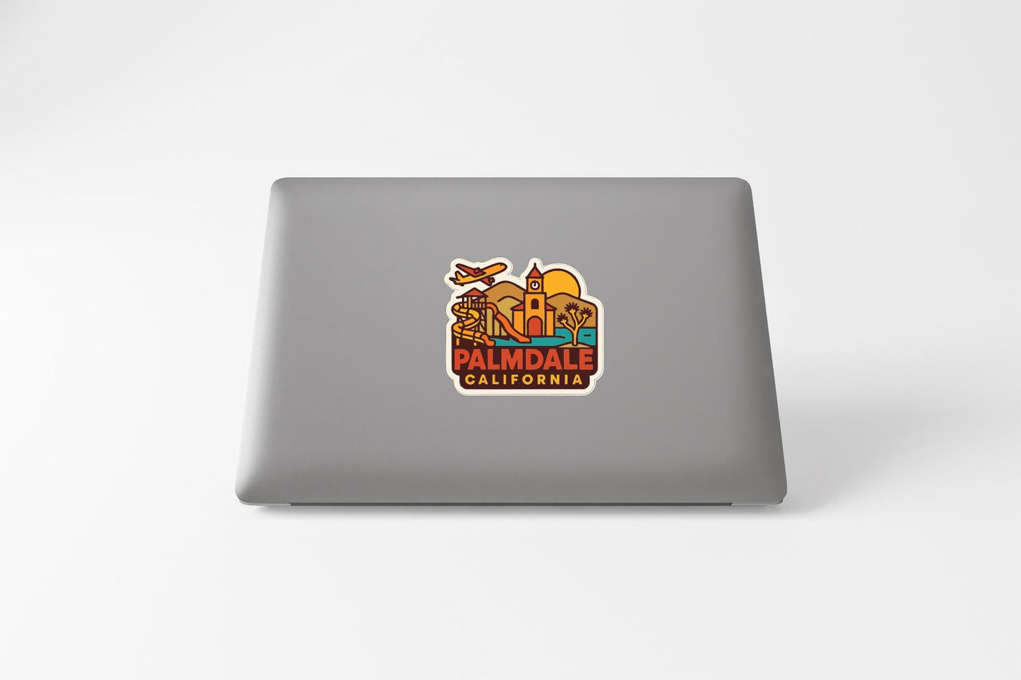 A sticker on the back of a laptop displaying the text "PALMDALE CALIFORNIA" along with various colorful illustrations of landmarks and symbols associated with the city of Palmdale, California.