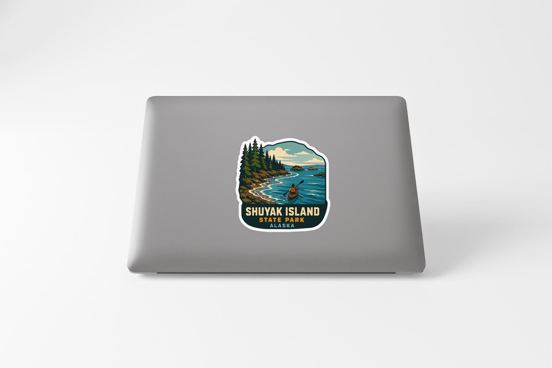A sticker on the back of a laptop, depicting a scenic landscape with a lake, mountains, and a person kayaking.