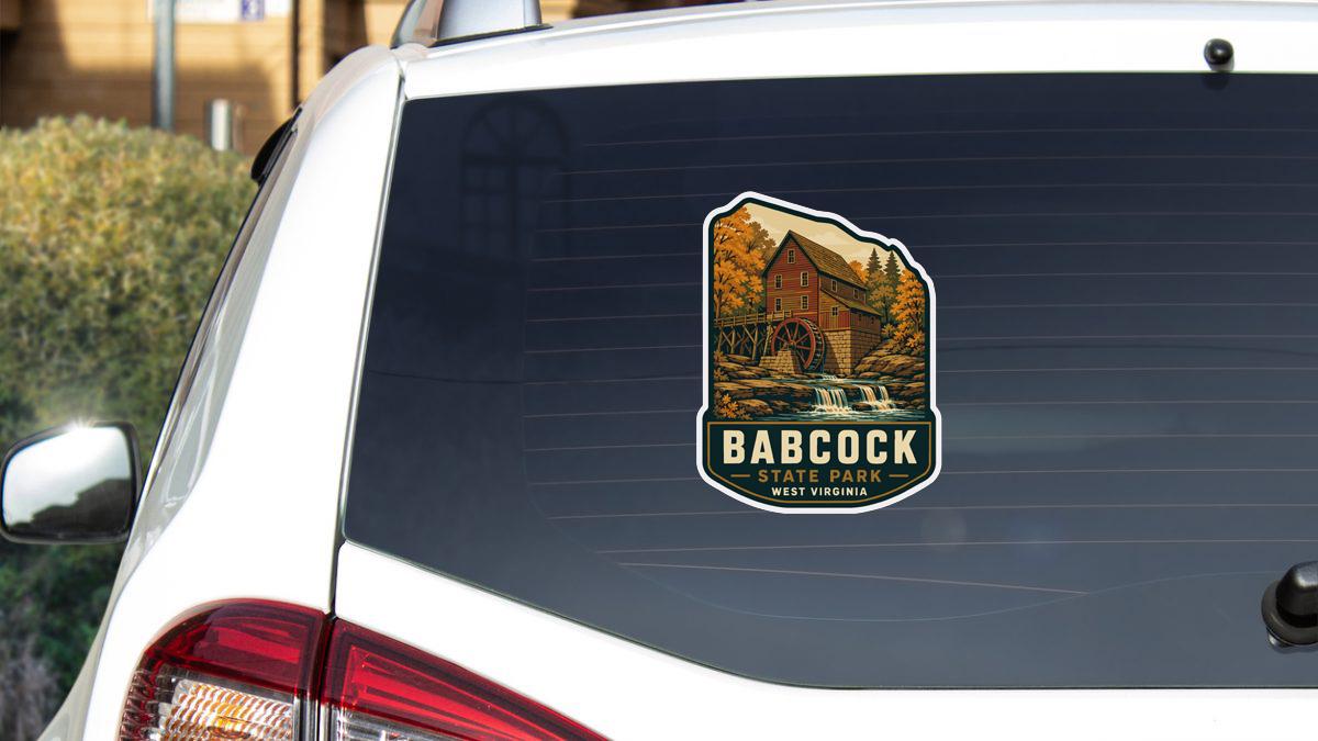 A sticker on the rear window of a white car, depicting a scenic landscape with a mill and a waterfall.