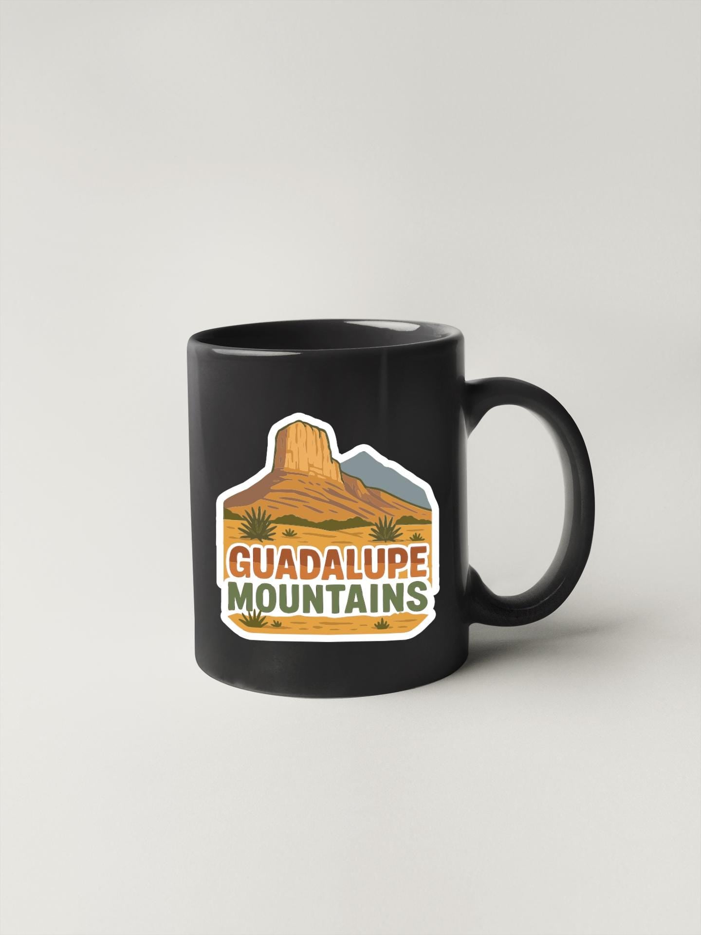 A black coffee mug with a graphic design featuring a mountain range and the text "GUADALUPE MOUNTAINS".