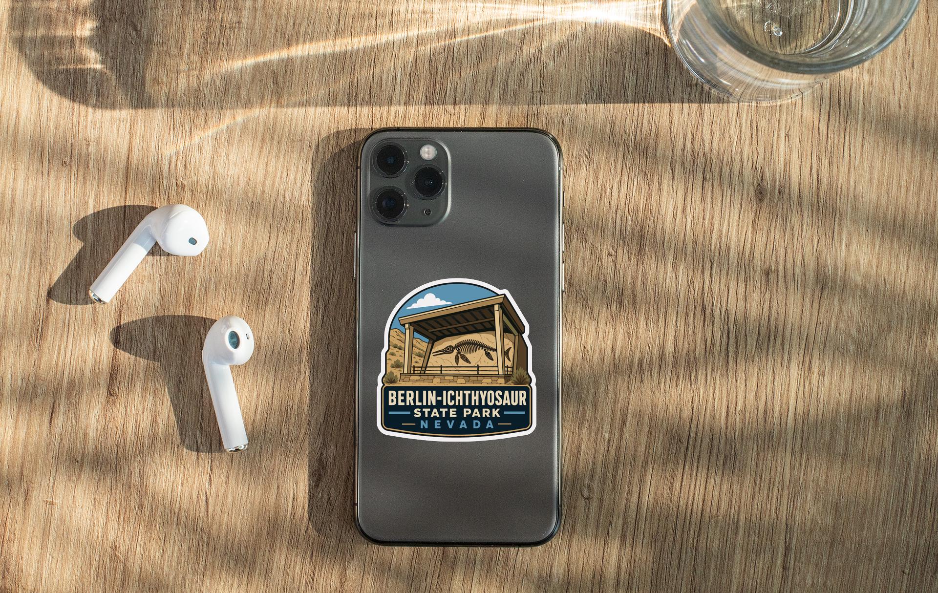 a smartphone with a sticker on the back, placed on a wooden surface alongside a pair of white earbuds and a glass of water.