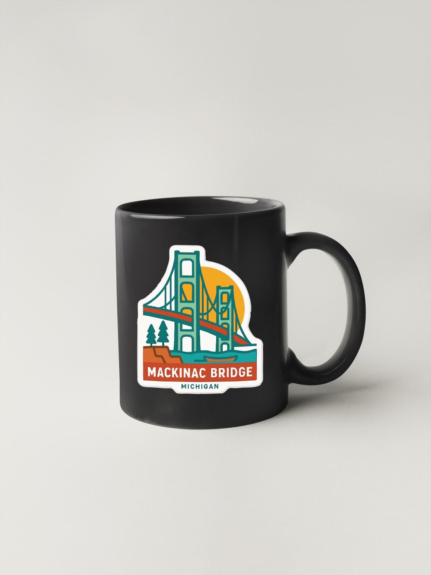 A black coffee mug with a graphic design depicting the Mackinac Bridge in Michigan.