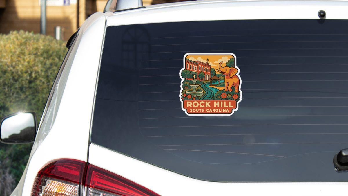 A sticker on the rear window of a white car, depicting a scenic view of Rock Hill, South Carolina.