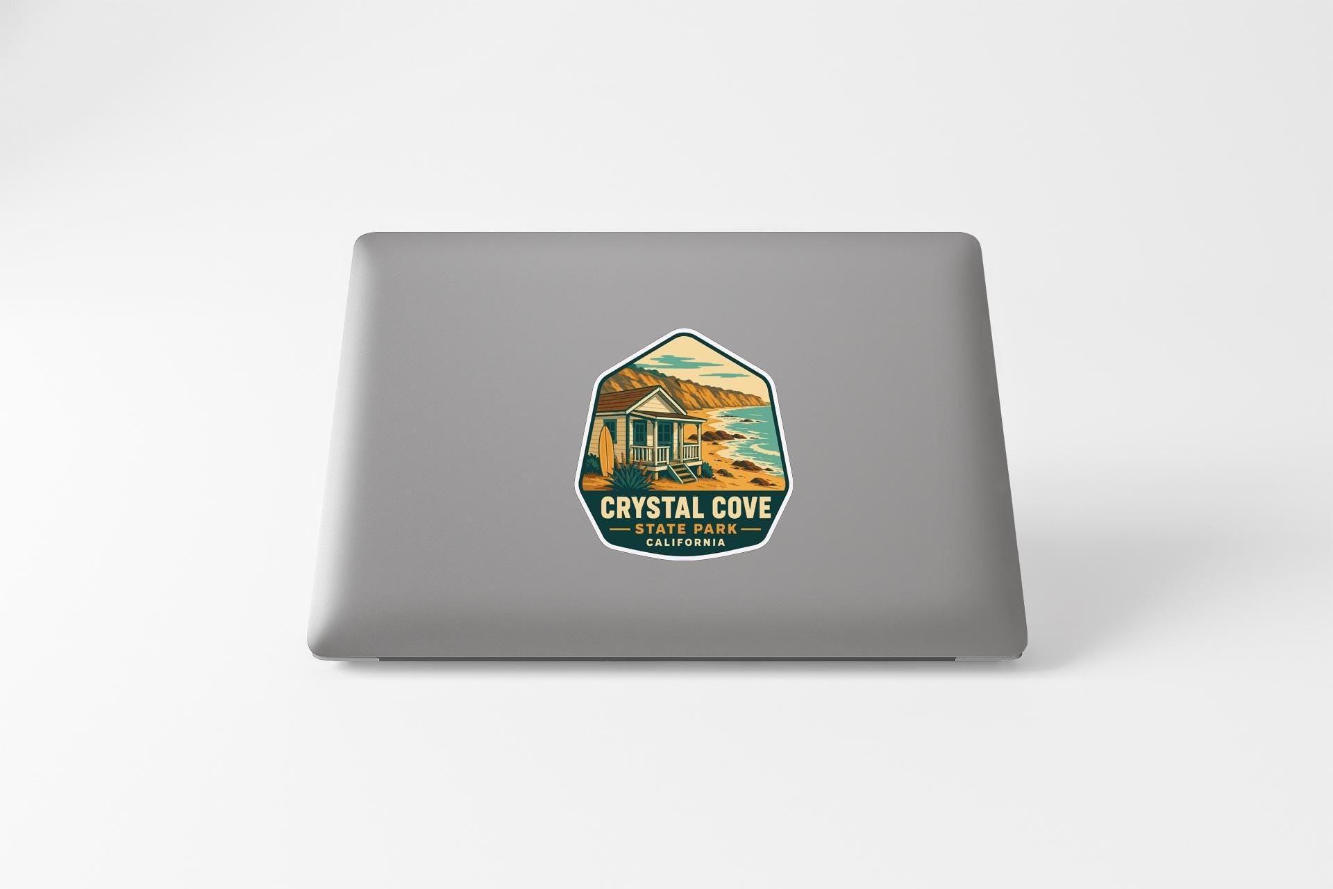 a sticker on the back of a laptop that displays a scenic coastal landscape with a house and mountains in the background.