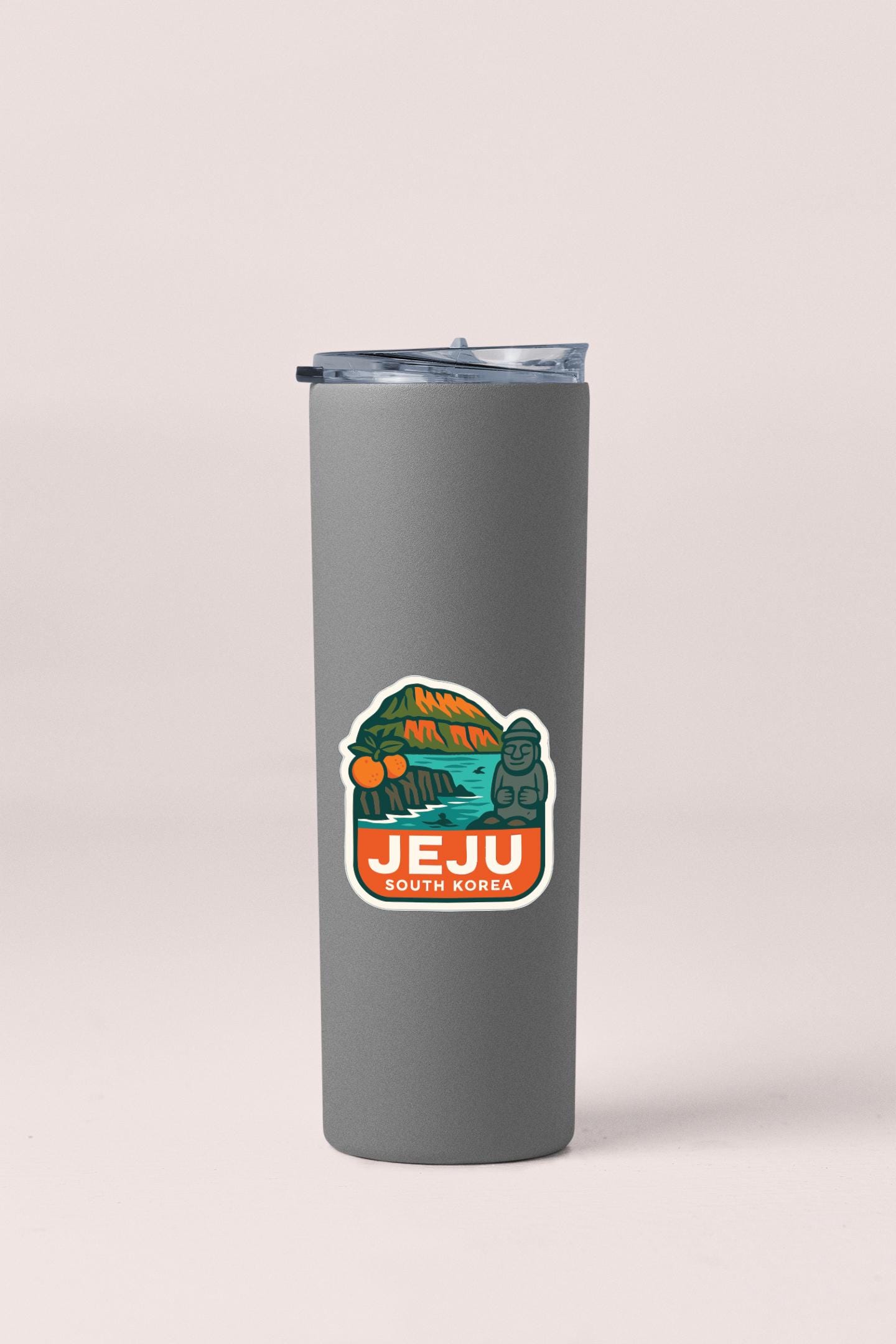 A gray insulated tumbler with a sticker on it, featuring an illustration of a mountain and text that says "Jeju South Korea".