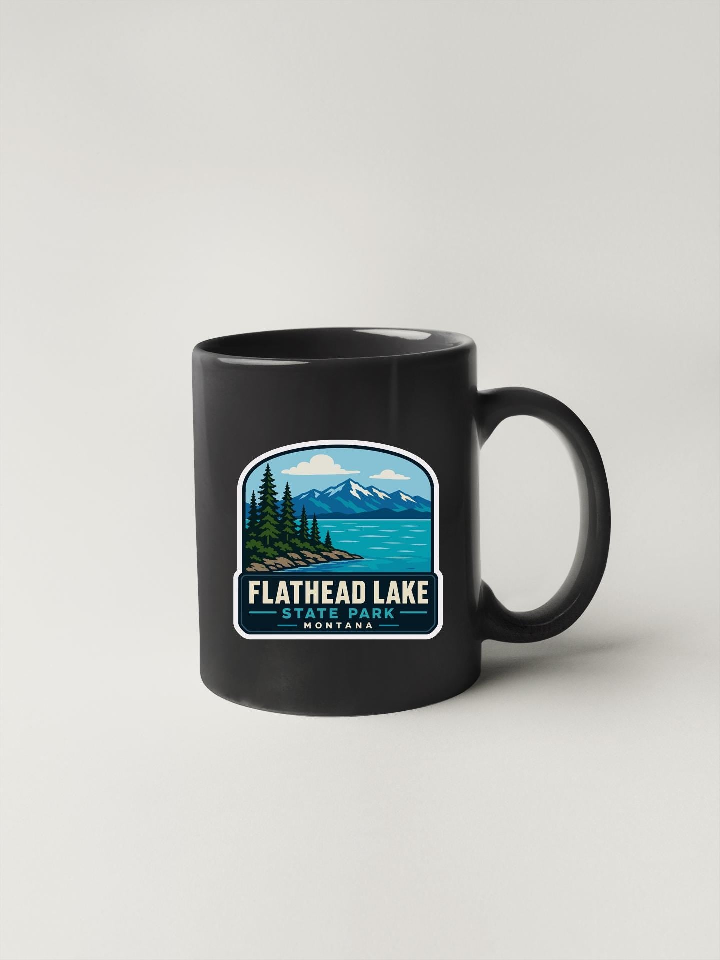 A black coffee mug with a graphic design depicting Flathead Lake State Park in Montana.