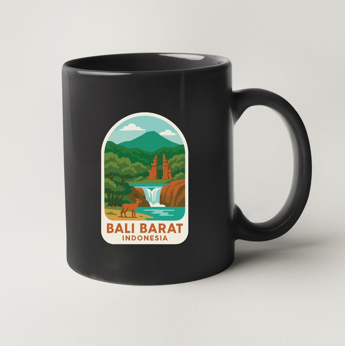 A black coffee mug with a sticker depicting a scenic landscape of Bali, Indonesia, featuring a waterfall, mountains, and a temple.