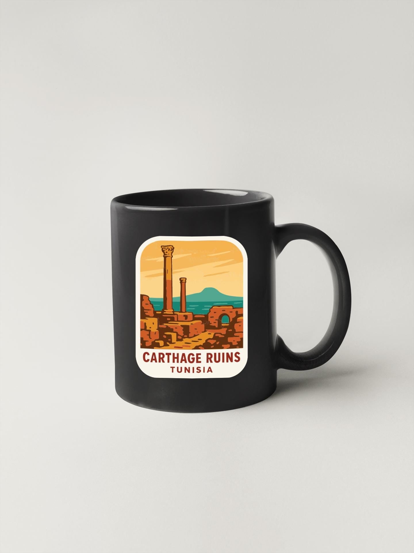 A black coffee mug with a sticker depicting the ancient city of Carthage, Tunisia.