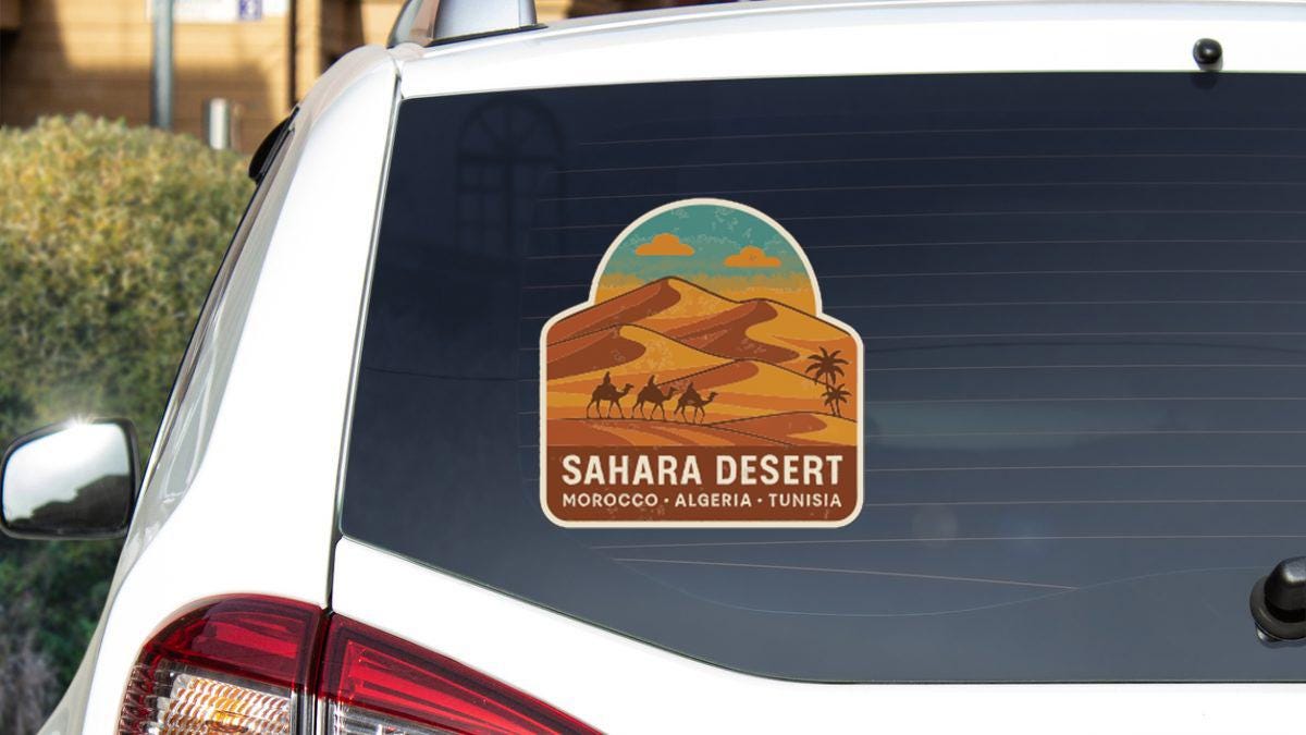 a sticker on the rear window of a car, depicting a desert landscape with sand dunes and a camel.