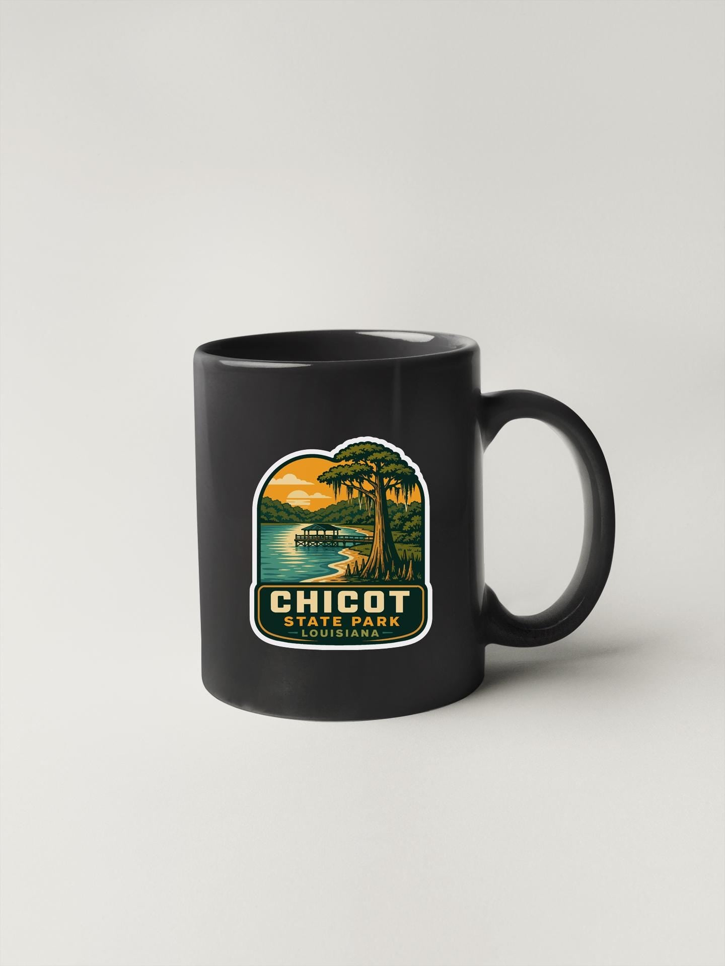 A black coffee mug with a sticker depicting a scenic landscape, including a lake, trees, and a sunset.
