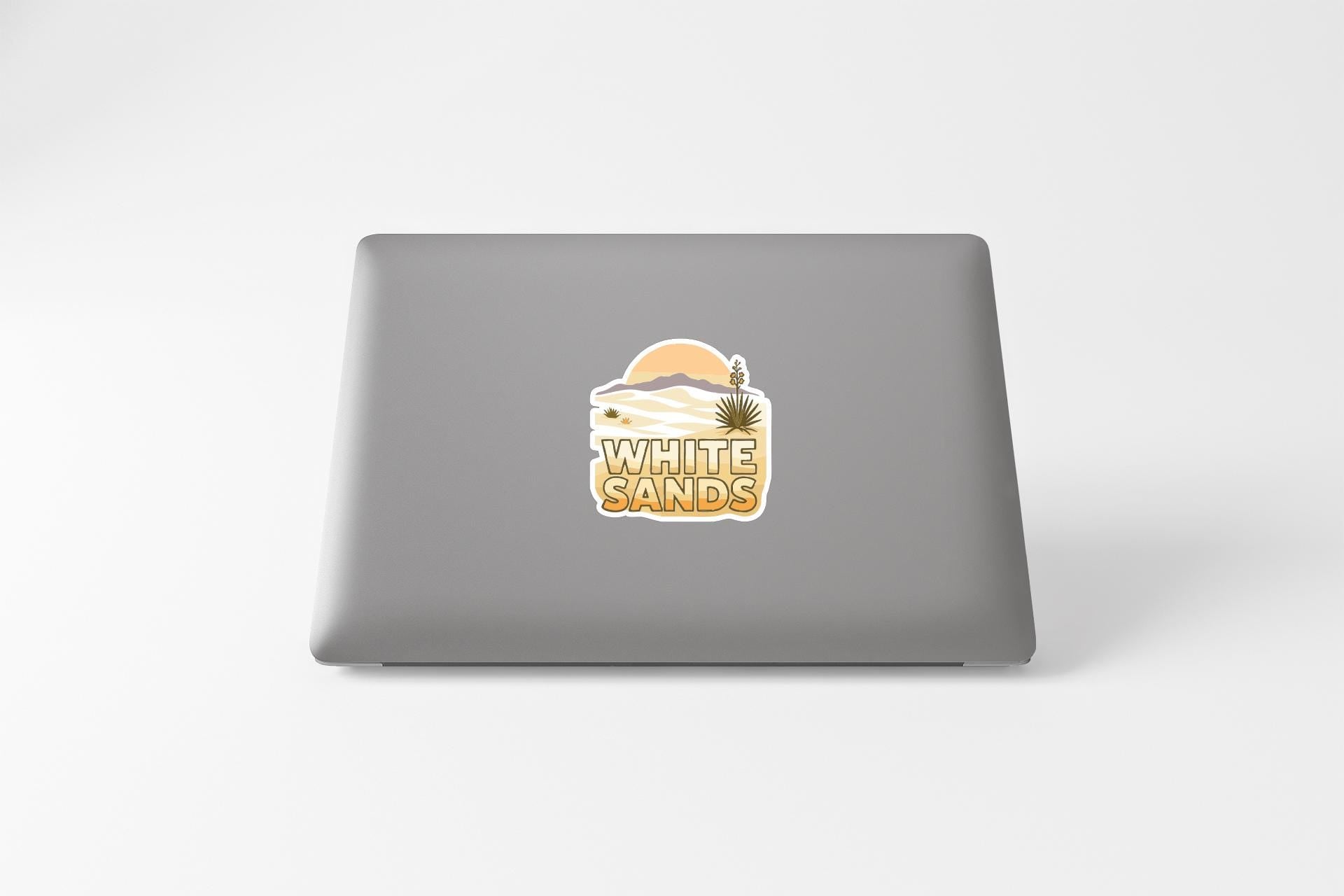 a sticker with a desert landscape and the text "WHITE SAND'S" on the back of a laptop.